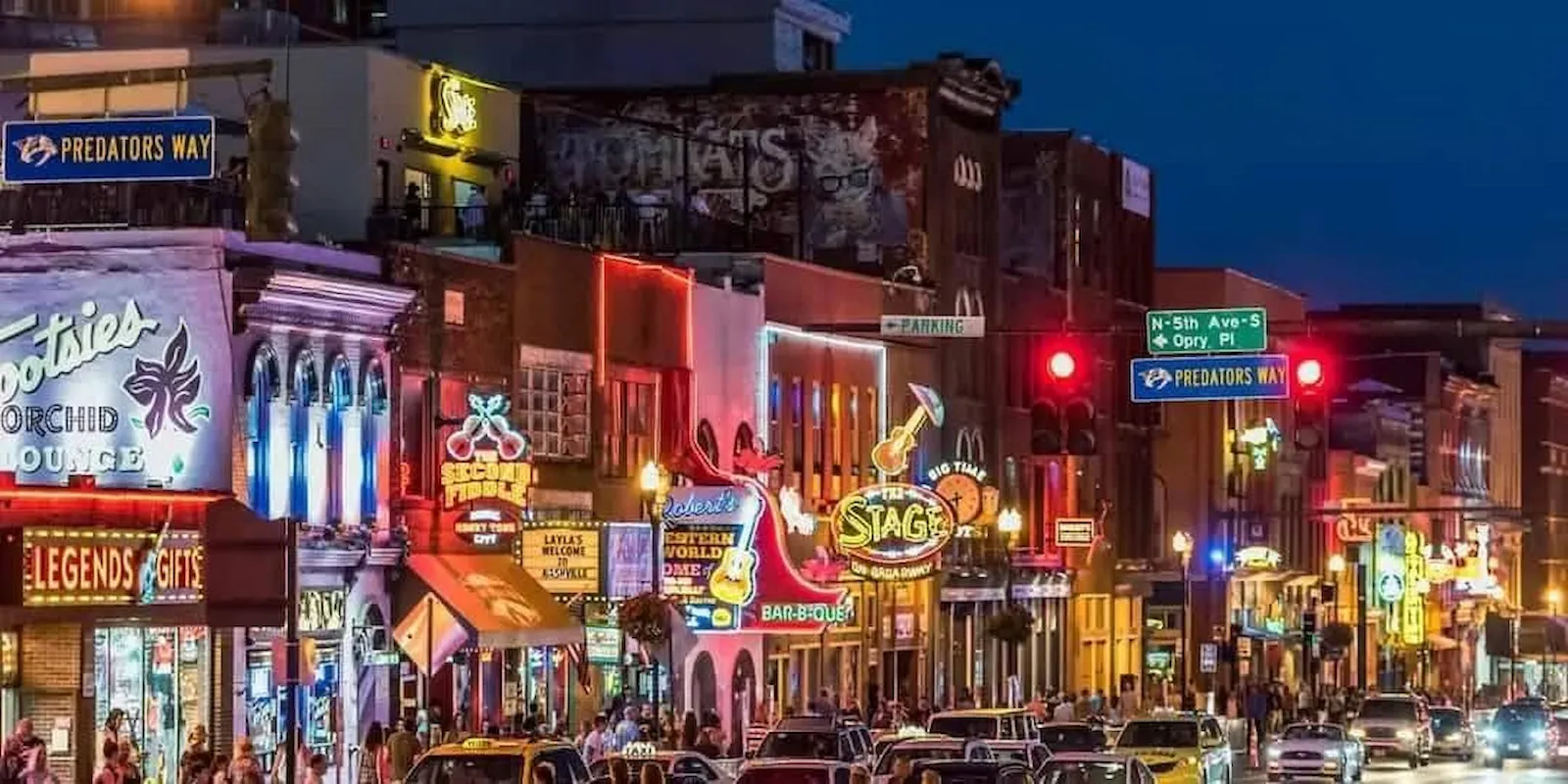 Nashville Broadway street at night with vibrant neon signs from honky-tonk bars including Tootsies Orchid Lounge and The Stage, showing the bustling nightlife of Music City
